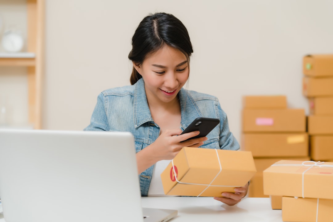 Woman checking package with phone near laptop and boxes